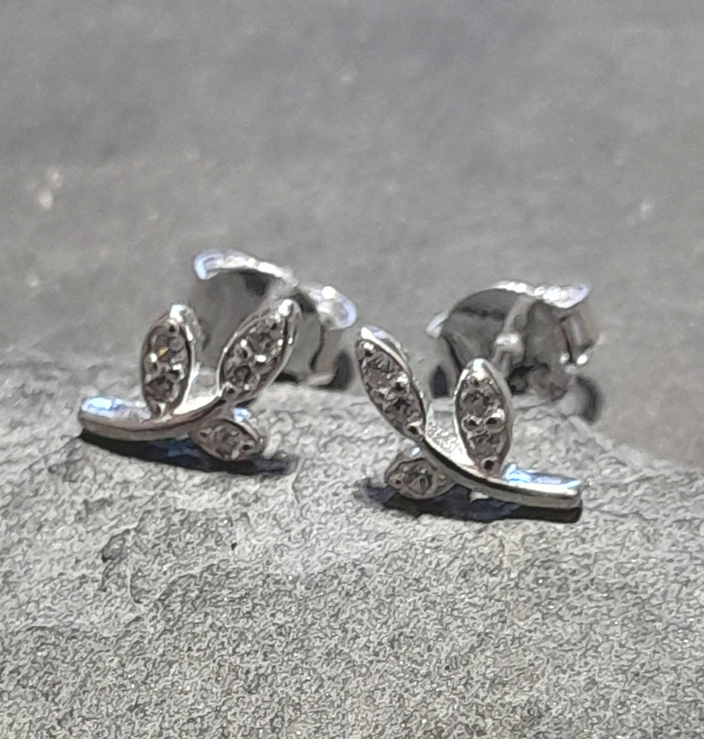 A pair of sterling silver earrings with clear cubic zirconia decorations in a branch pattern, displayed on a textured grey background.